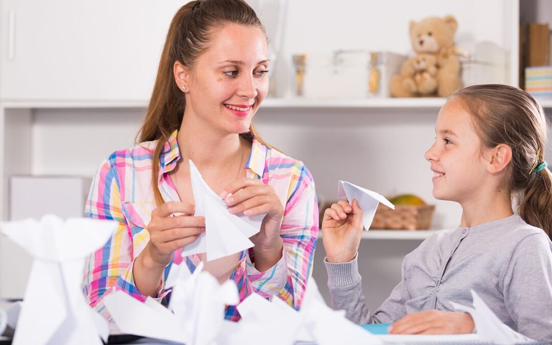 Une maman et sa fille plient des avions en papier ensemble à la maison