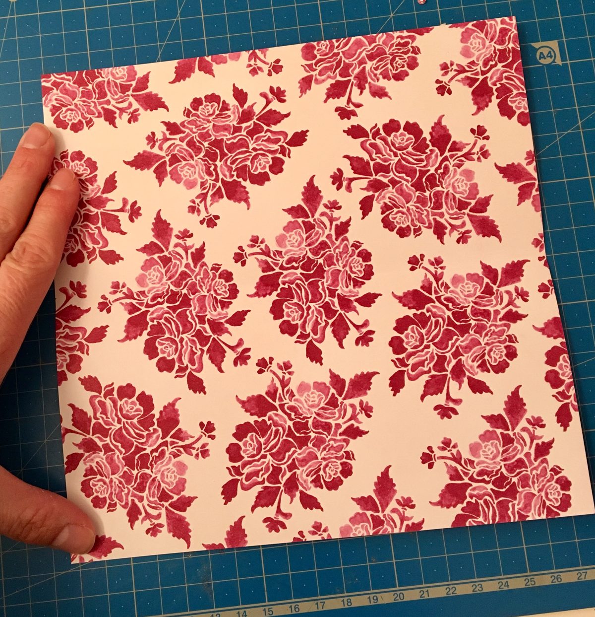 Feuille de papier carrée à motif posée sur un tapis de découpe, prête pour le pliage