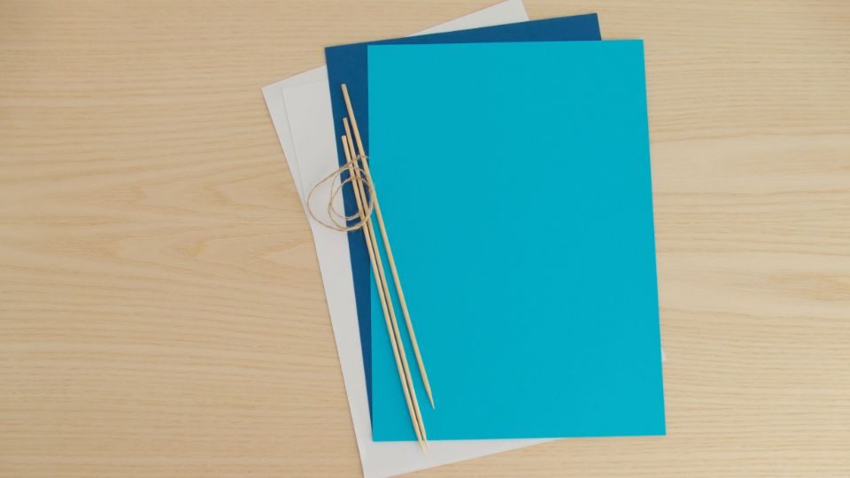 Le matériel pour plier un bateau en papier : feuilles de couleur et pics en bois