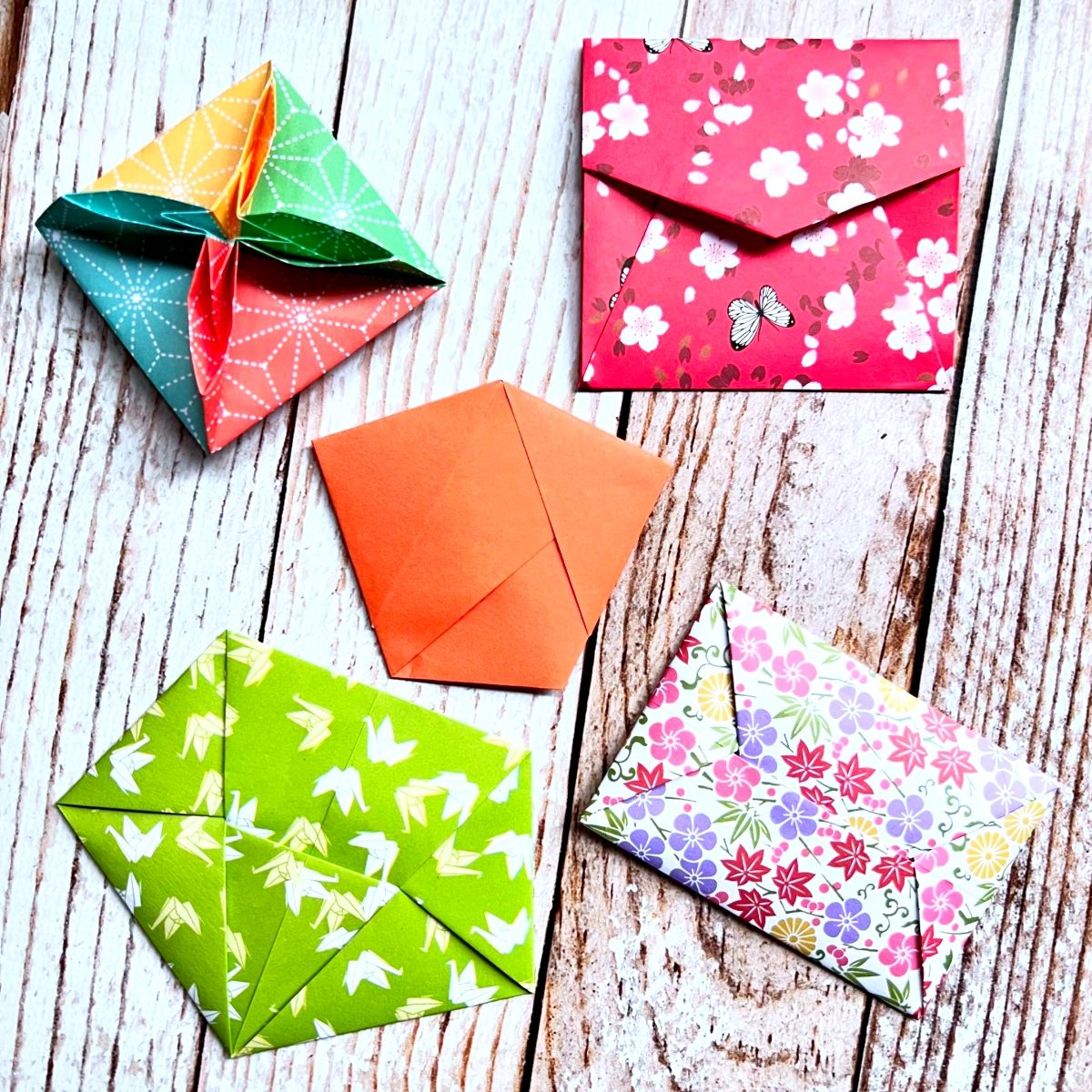 Plusieurs enveloppes en origami en papier à motifs colorés posées sur du bois