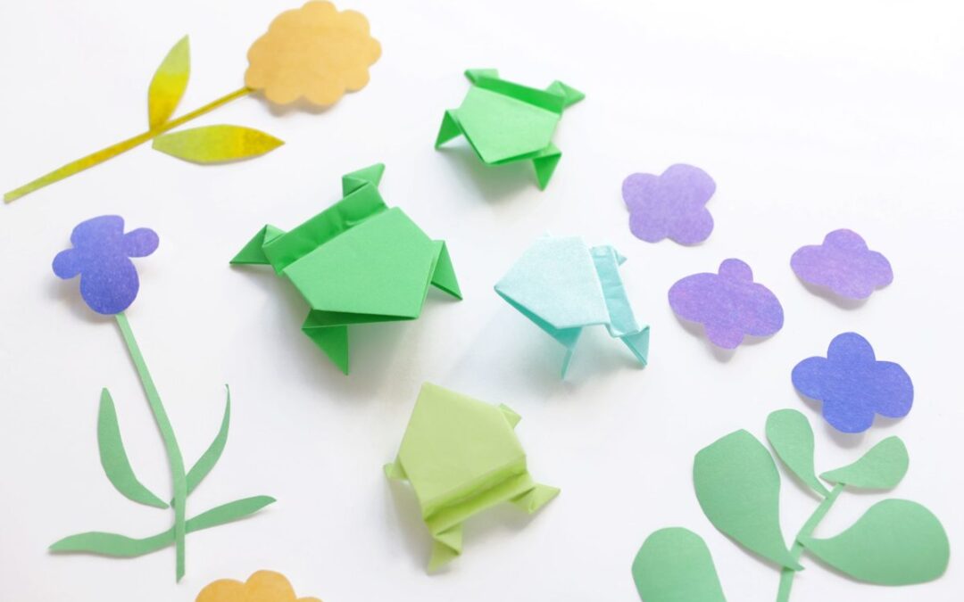 Grenouilles en origami colorées posées parmi des fleurs en papier