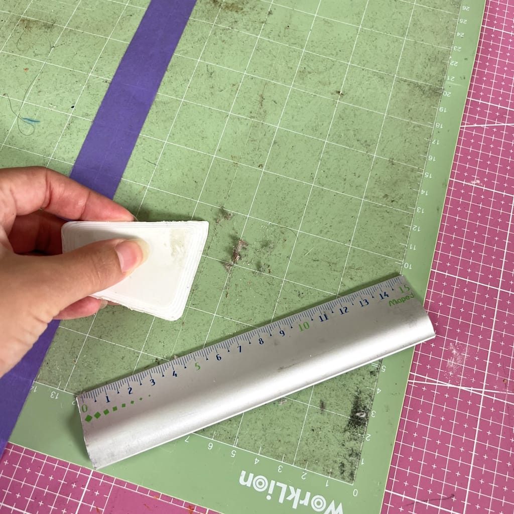 Gratter les résidus d'un tapis de découpe avec une spatule plastique, les bords protégés par du masking tape