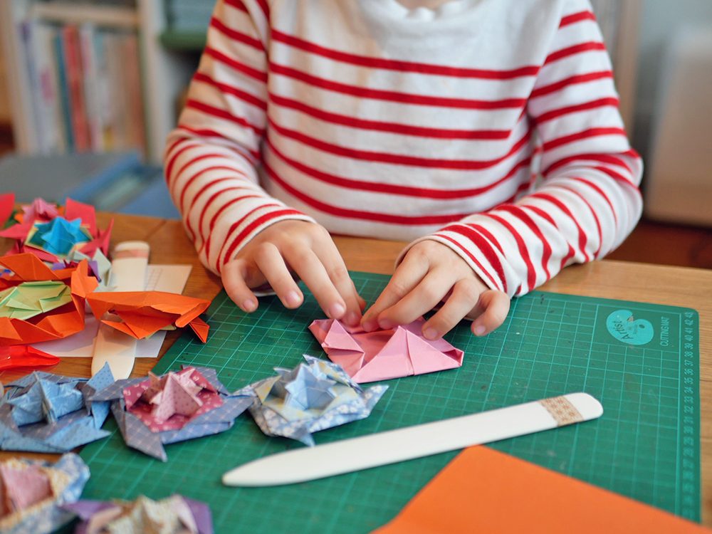 Enfant en train de plier une toupie en papier avec un plioir