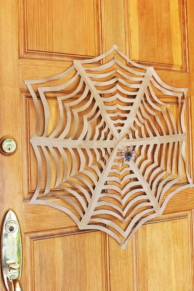Grande toile d'araignée découpée dans du papier kraft, accrochée à une porte en bois