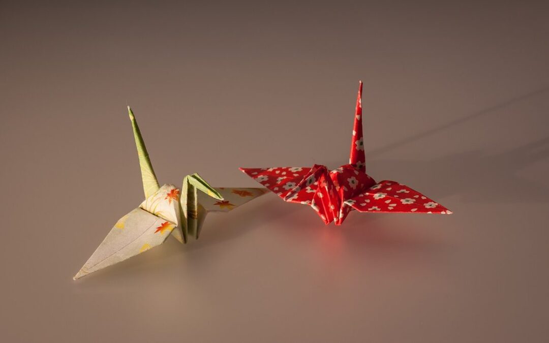 Deux grues en origami pliées dans du papier washi coloré, posées sur un fond chaud