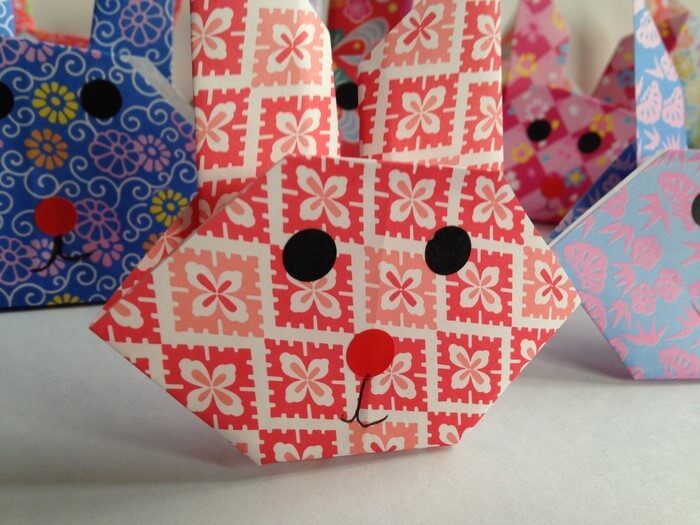 Plusieurs têtes de lapin en origami pliées dans des papiers japonais à motifs, avec des yeux et un museau dessinés