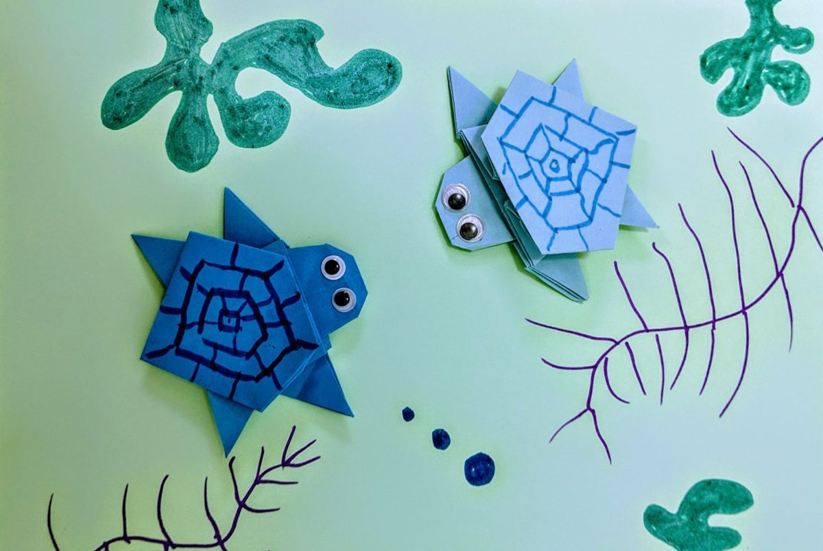 Deux petites tortues en origami bleues avec des yeux mobiles sur un décor marin dessiné