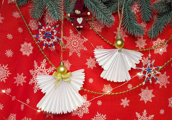 Deux anges de Noël en papier blanc plissé en éventail, avec une tête en perle dorée, suspendus devant un fond rouge à flocons