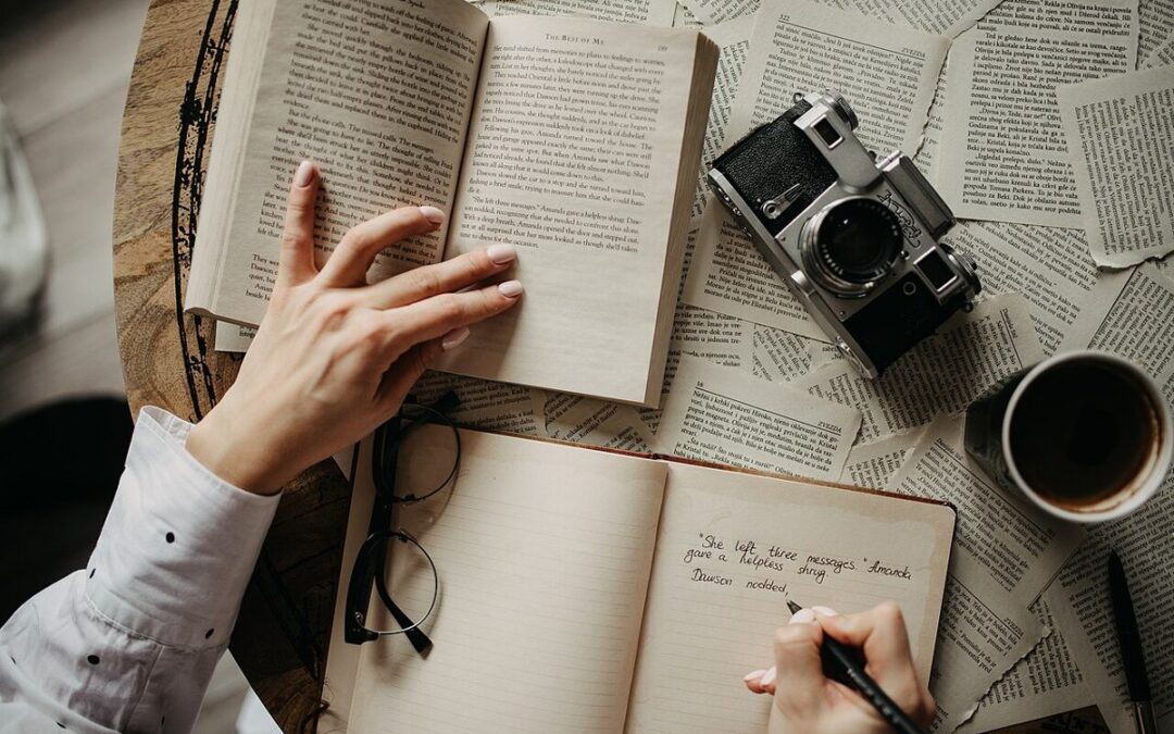 Une main qui écrit dans un carnet de lecture, un livre ouvert à côté
