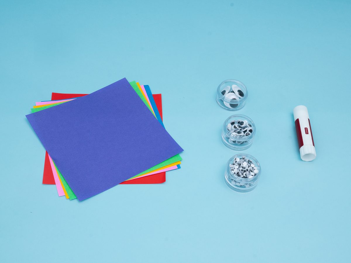 Feuilles de papier colorées, ciseaux et colle posés sur une table pour fabriquer un marque-page coin