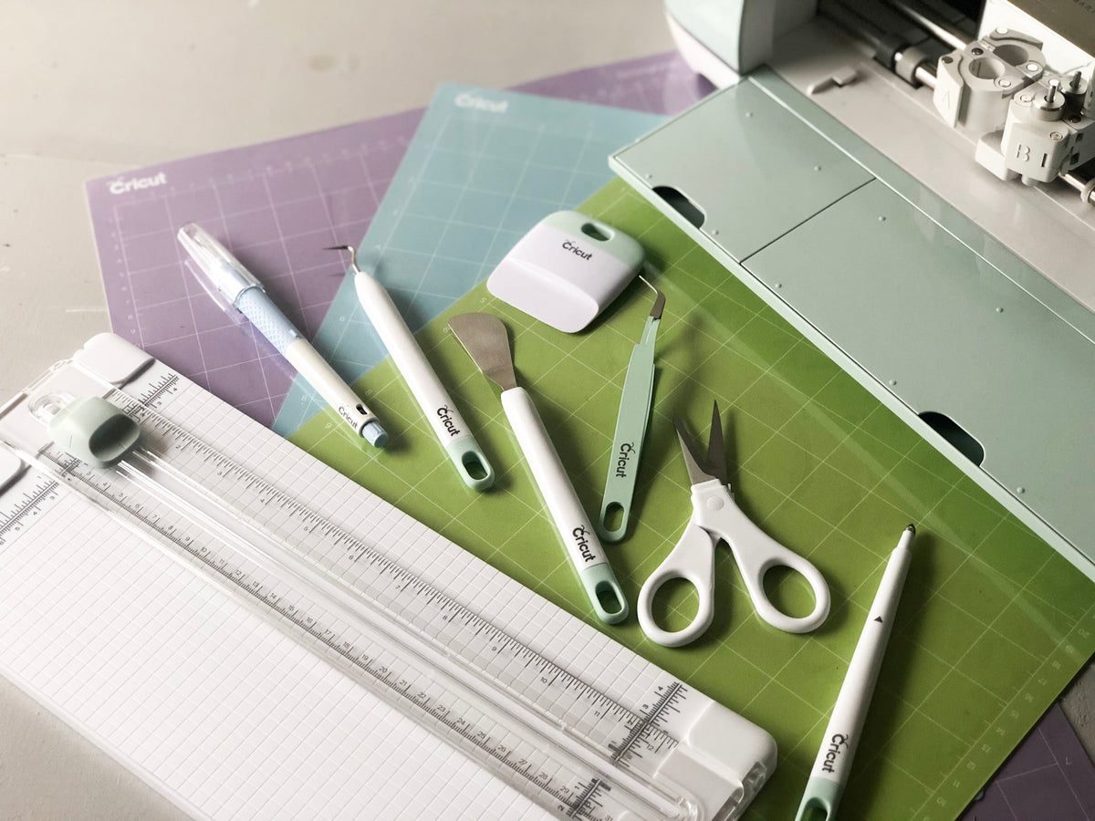 Outils Cricut et tapis de decoupe bleu, violet et vert autour d'une machine Cricut Maker